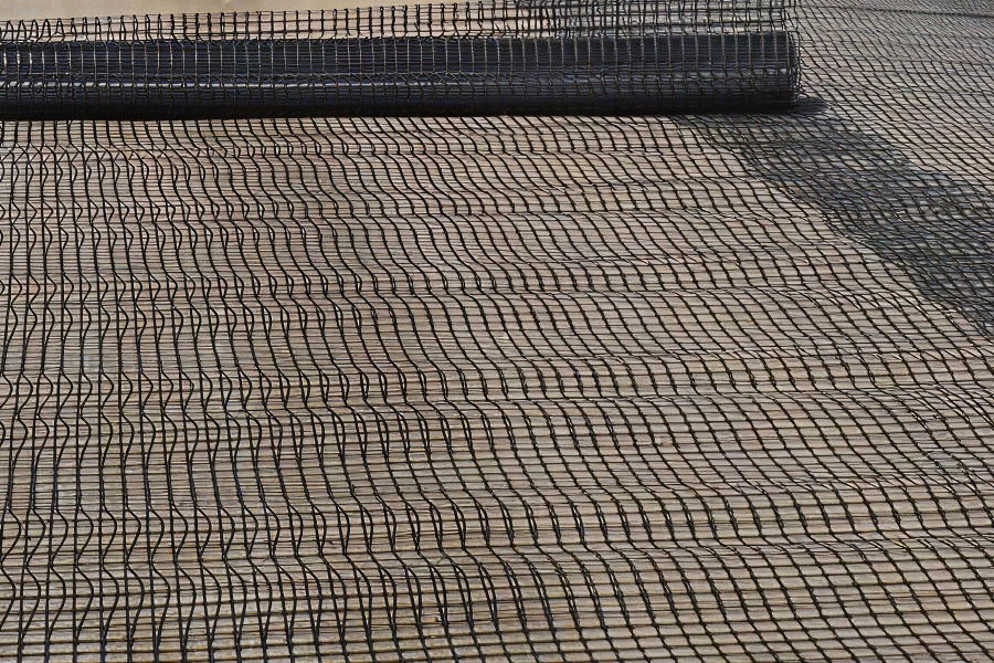 A roll of black geogrid material laid out on a surface, showing its interwoven pattern.