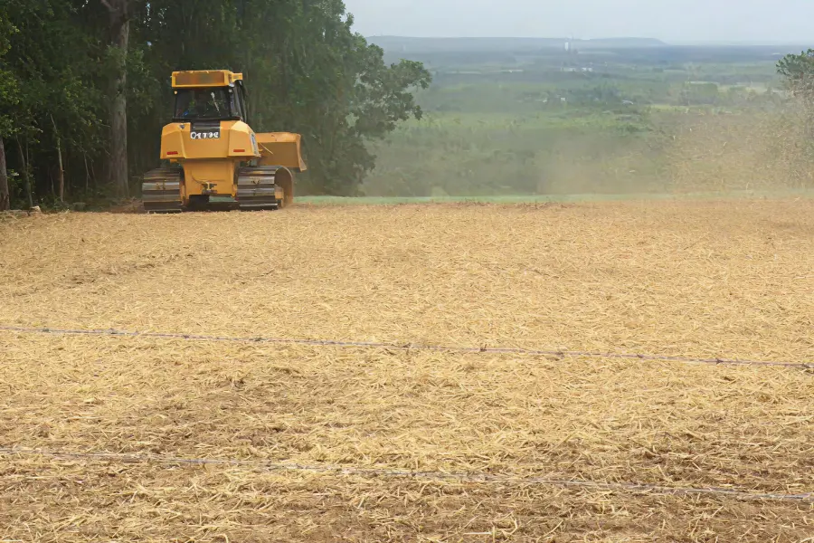 A yellow tractor applies straw mulch to a field using tackifier for erosion control