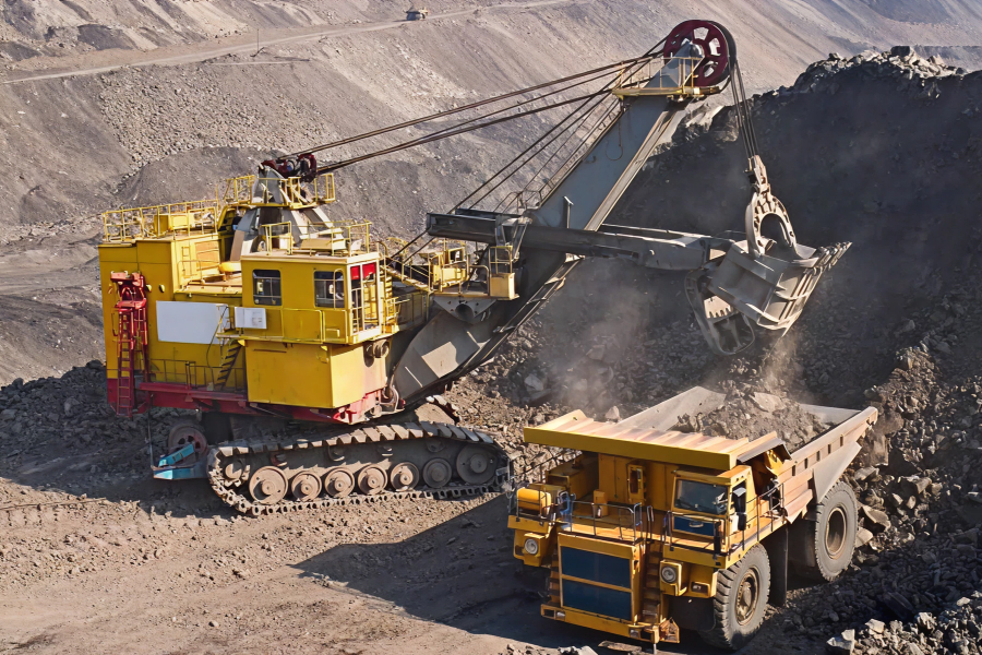 Large yellow mining excavator loading rock and dirt into an equally large yellow dump truck in an open-pit mine.