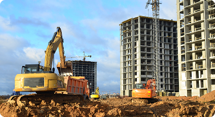 Construction site with multiple excavators on dirt, and several unfinished concrete high-rise buildings and cranes in the background.