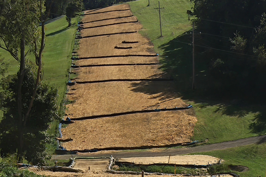 Terraced hillside covered in wood chips with compost filter socks for erosion control, alongside green grass and trees.