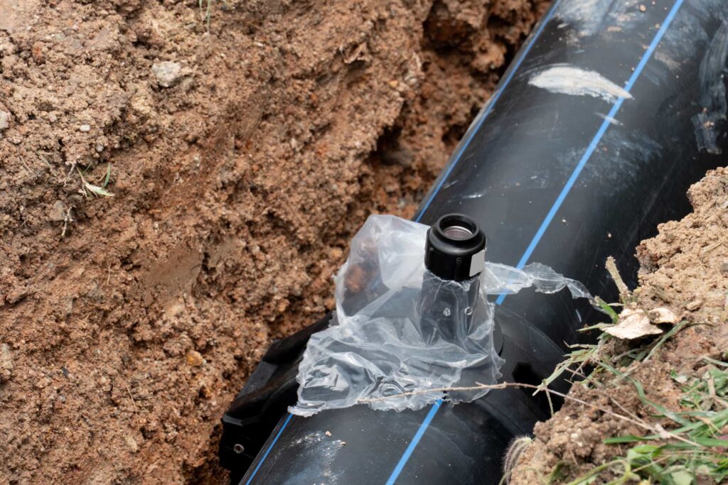Black pipe with blue stripe in a trench, showing a connection point covered in plastic.