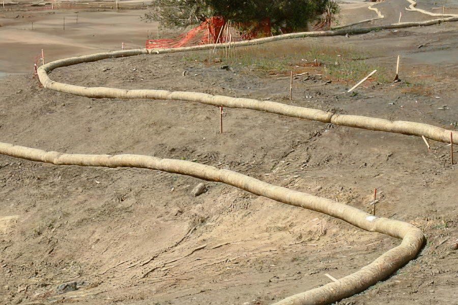 Erosion control logs installed on a muddy construction site to prevent soil runoff, with wooden stakes securing them.